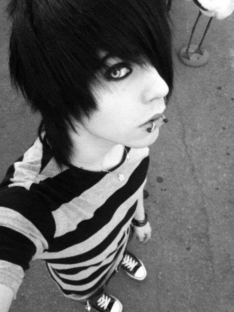 Emo — czarno-białe zdjęcie chłopaka z długą czarną grzywką zasłaniającą oko, eyelinerem, kolczykiem w wardze i w koszulce w poziome pasy